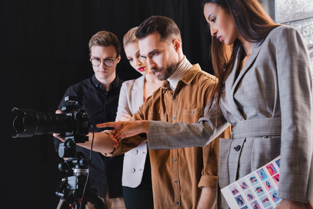 photographer, model, stylist and producer looking at digital camera on backstage